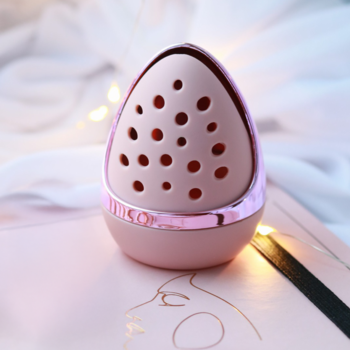 Zbliżenie na różowe, jajowate etui na gąbkę do makijażu z metalicznym wykończeniem i perforacjami.