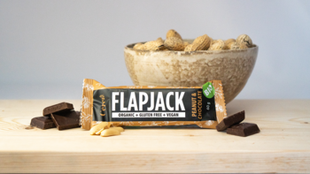 Baton owsiany FLAPJACK organiczny, z orzeszkami ziemnymi i czekoladą, widok z przodu, na drewnianym blacie.