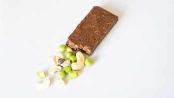 Ekologiczny wegański baton proteinowy czekoladowy bezglutenowy, obok nerkowce i edamame, widok z góry.