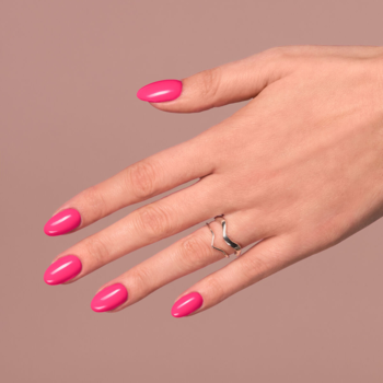Dłoń z neonowym malinowym lakierem do paznokci. Półkryjący efekt, długie, owalne paznokcie. Tło beżowe.