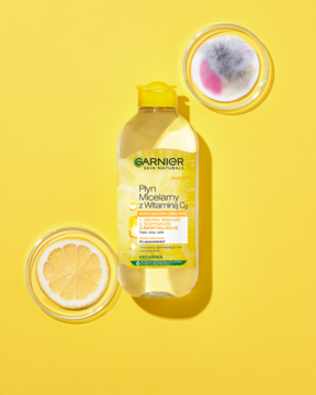 Garnier Płyn Micelarny z Witaminą Cg, żółta butelka na żółtym tle. Obok plaster cytryny i zużyty wacik.