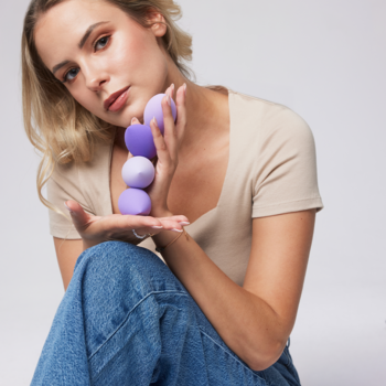 Młoda kobieta trzyma fioletowe gąbki do makijażu do podkładu. Trzy gąbki w kształcie łezki, różne odcienie fioletu.