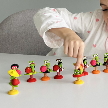 Bob Snail Eat&Play zestaw: dziecko dotyka jednej z rzędu kolorowych figurek ślimaków na białym stole.