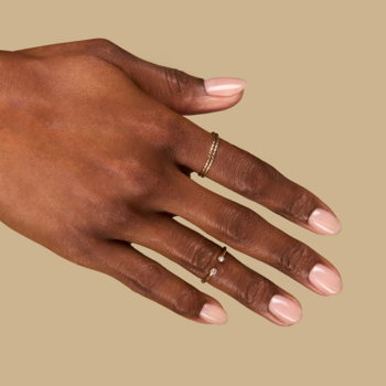 Zbliżenie dłoni z naturalnym, półtransparentnym beżowym lakierem Second Skin Nude i delikatnymi pierścionkami.