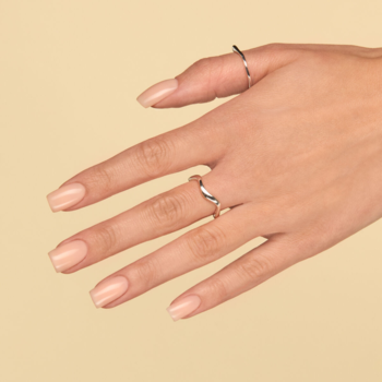 Dłoń z paznokciami pomalowanymi półtransparentnym, beżowym lakierem Just Nude. Na palcach dwa srebrne pierścionki.