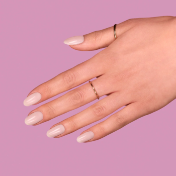 Dłoń z jasnoróżowymi, owalnymi paznokciami i dwoma cienkimi złotymi pierścionkami na fioletowym tle.