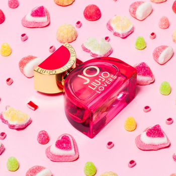 Liu Jo Lovers: czerwony flakon perfum ze złotą nakrętką, otoczony kolorowymi cukierkami na różowym tle.