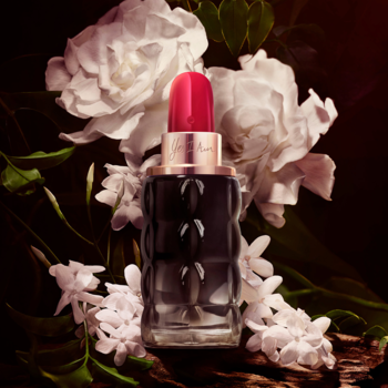 Perfumy Cacharel Yes I Am owocowo-kwiatowe. Ryflowany flakon z czerwonym korkiem na tle białych kwiatów.