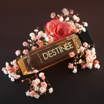 DESTINÉE woda perfumowana orientalno-fougère, złota butelka z czarnym korkiem, różowa róża i kwiaty na ciemnym tle.