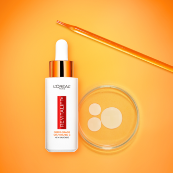L'Oréal Revitalift Clinical serum z witaminą C, butelka z pipetą, krople na szkiełku, na pomarańczowym tle.