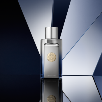 Antonio Banderas The Icon Elixir, srebrna butelka męskich perfum z złotą monetą, na tle geometrycznych tafli.