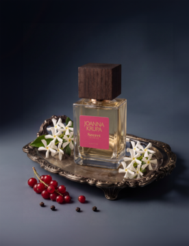 Perfumy Joanna Krupa Secret Sense w butelce z drewnianym korkiem, na srebrnej tacy z czerwonymi porzeczkami i jaśminem.