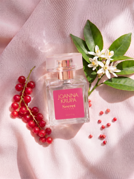 Perfumy Joanna Krupa Secret Sense, elegancka butelka na różowej tkaninie, z czerwoną porzeczką i neroli.