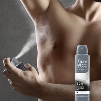 Mężczyzna aplikuje szary antyperspirant w sprayu Dove MEN+CARE Invisible Dry 72H pod pachę. Druga puszka obok.