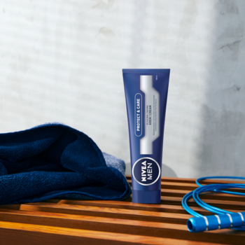 NIVEA MEN Protect & Care krem do golenia w niebieskiej tubce, stojący na drewnianej ławce z ręcznikiem i skakanką.