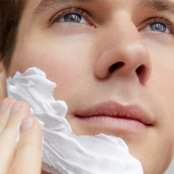 NIVEA MEN Protect & Care Pianka do golenia. Mężczyzna nakłada białą, puszystą piankę na policzek. Zbliżenie.