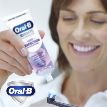 Uśmiechnięta kobieta wyciska pastę Oral-B 3D White Advanced Luxe Perfection z białej tubki na szczoteczkę elektryczną Oral-B.