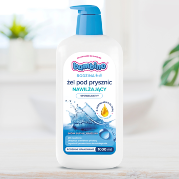 Biała butelka Bambino Family 1000ml, nawilżający żel pod prysznic z niebieską pompką, na rozmytym tle łazienki.
