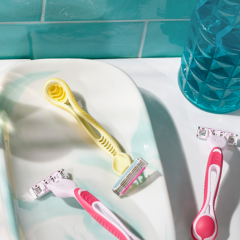 Trzy jednorazowe maszynki Gillette Venus 3 Dragonfruit: żółta i dwie różowe, leżą na zlewie z niebieskim tłem.