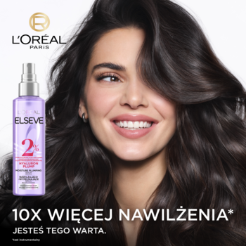 Uśmiechnięta kobieta z bujnymi włosami prezentuje L'Oréal Elseve Hyaluron Plump serum w fioletowej butelce spray.