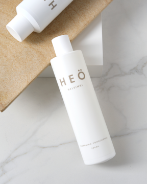 Biała butelka Heö Cleansing Conditioner, widok z góry na marmurowym tle, z brązowym napisem Heö Helsinki.