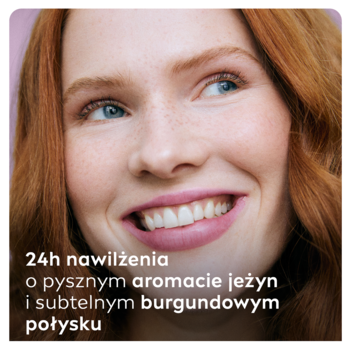 Uśmiechnięta kobieta z rudymi włosami, usta z jeżynowym kolorem NIVEA Blackberry Shine i delikatnym połyskiem.