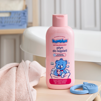Różowa butelka Bambino Płyn do Kąpieli dla dzieci z grafiką misia, na drewnianej podstawce, w tle wanienka.