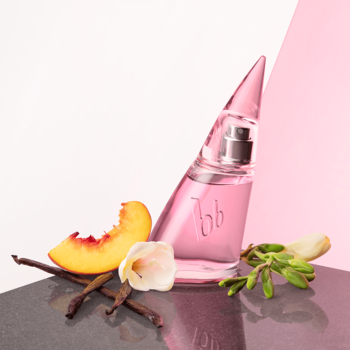 Różowa butelka bruno banani Original EDT szyprowo-owocowa, ukośnie, z brzoskwinią, wanilią i kwiatami na tle różu.