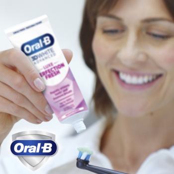 Pasta wybielająca Oral-B 3D White Luxe Perfection Fresh wyciskana na szczoteczkę, z uśmiechniętą kobietą w tle.