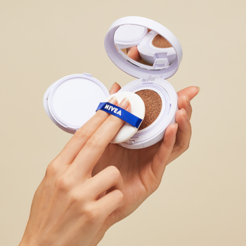 Otwarty NIVEA Cellular 3w1 podkład w poduszce SPF15. Ręka z aplikatorem dotyka jasnego kosmetyku.