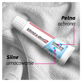 Klej do protez Blend-a-dent Complete Strong Hold, biała tuba z niebiesko-czerwonym logo, na białym ręczniku.