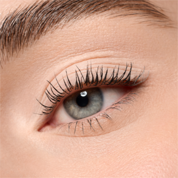 Zbliżenie na kobiece oko z gęstymi, podkręconymi rzęsami, które podkreślają szaro-niebieską tęczówkę. Naturalny makijaż.