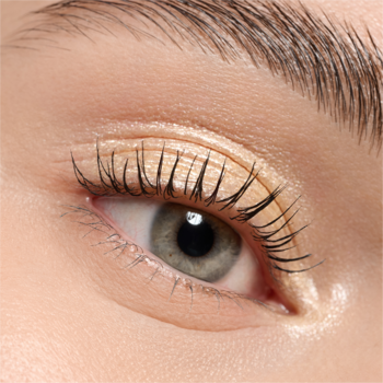 Zbliżenie na otwarte, ludzkie oko z zielono-szarą tęczówką. Widoczne pomalowane rzęsy i jasny, perłowy cień na powiece.