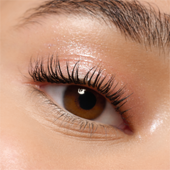 Zbliżenie na otwarte brązowe oko z długimi, ciemnymi rzęsami i naturalnie lśniącą powieką.