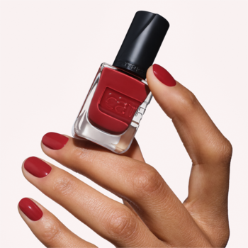 Ręka z czerwonym manicure trzyma lakier Catrice GEL AFFAIR 057 Signature Bloom w odcieniu brązowej czerwieni, żelowy.