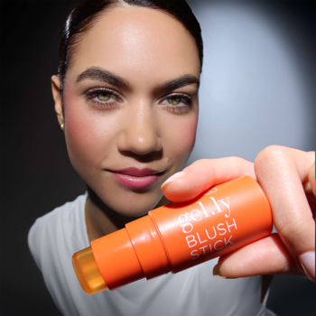 Modelka z naturalnym rumieńcem prezentuje pomarańczowy żelowy róż Artdeco Gel.ly Blush Stick, trzymając go do obiektywu.