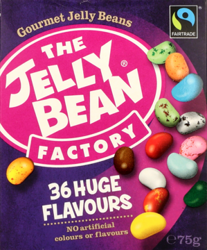 Front opakowania The Jelly Bean Factory Gourmet Jelly Beans, fioletowo-różowe, z rozsypanymi kolorowymi fasolkami.