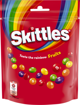 Cukierki Skittles Fruits w czerwonej torebce z tęczowym paskiem, widok z przodu, z rozsypanymi owocowymi cukierkami.
