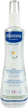 Biała butelka Mustela Hair Styler & Skin Freshener w sprayu, z niebieską etykietą i rumiankiem, widok z przodu.