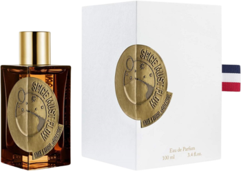 Bursztynowa butelka perfum Spice Must Flow Etat Libre d’Orange obok otwartego białego pudełka.