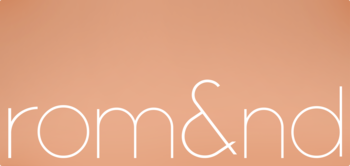 Logo marki rom&nd: cienkie, białe litery na gładkim brzoskwiniowym tle, minimalistyczny design firmy kosmetycznej.