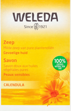 Z przodu żółte opakowanie mydła Weleda Calendula do skóry wrażliwej, z pomarańczowymi kwiatami i logo 100% naturalne.