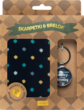 Zestaw prezentowy Soxo w brązowym pudełku: granatowe skarpetki w kropki i brelok z napisem o skromności, widok z przodu.