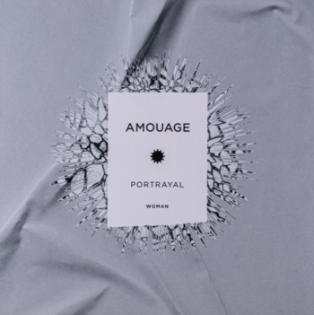 Amouage Portrayal Woman, biała etykieta otoczona rozbitym szkłem na tle szarej, pogniecionej tkaniny.
