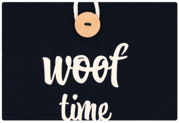 Czarny dekoracyjny szyld z białym napisem "woof time" w ozdobnej czcionce i drewnianym guzikiem u góry.