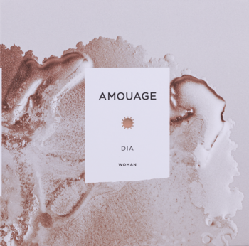Amouage Dia Woman perfumy, zbliżenie na białą etykietę z czarnym tekstem, tło z płynnym wzorem rose gold.