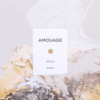 Biała etykieta Amouage Gold Woman z złotym emblematem, na tle abstrakcyjnych, luksusowych złotych i szarych smug.