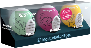 Trzy jajka Satisfyer Masturbator Eggs: zielone Riffle, różowe Bubble, żółte Fierce, w ekspozytorze, różne tekstury.