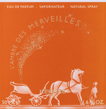Pomarańczowe opakowanie perfum Hermes L'Ambre Des Merveilles, z grafiką białego konia, karety i iskrzących gwiazd.