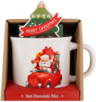 Biały kubek z Mikołajem w czerwonej ciężarówce, w opakowaniu z zestawem waniliowej czekolady do picia.